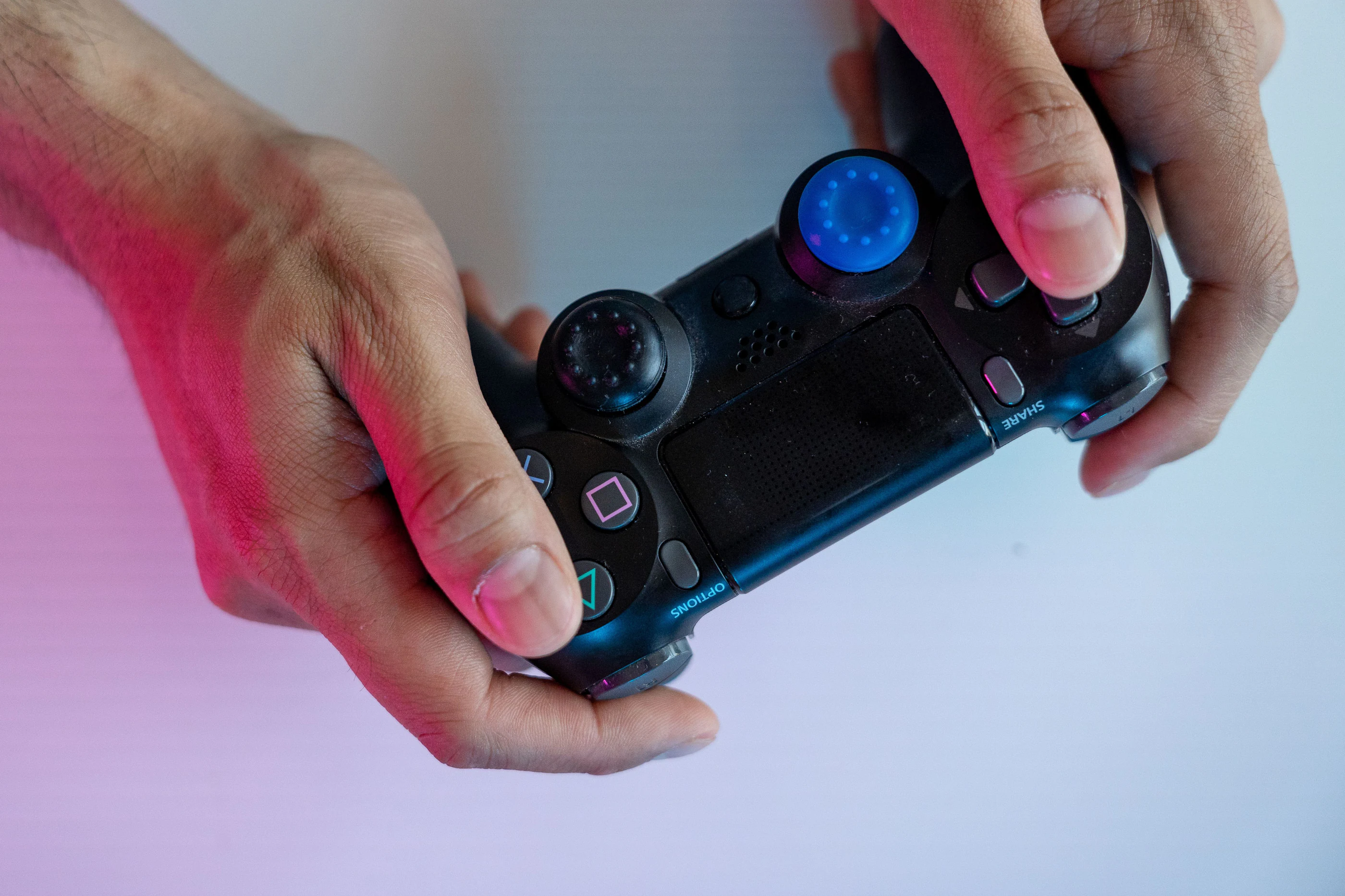 Hands on a game controller under coloured light