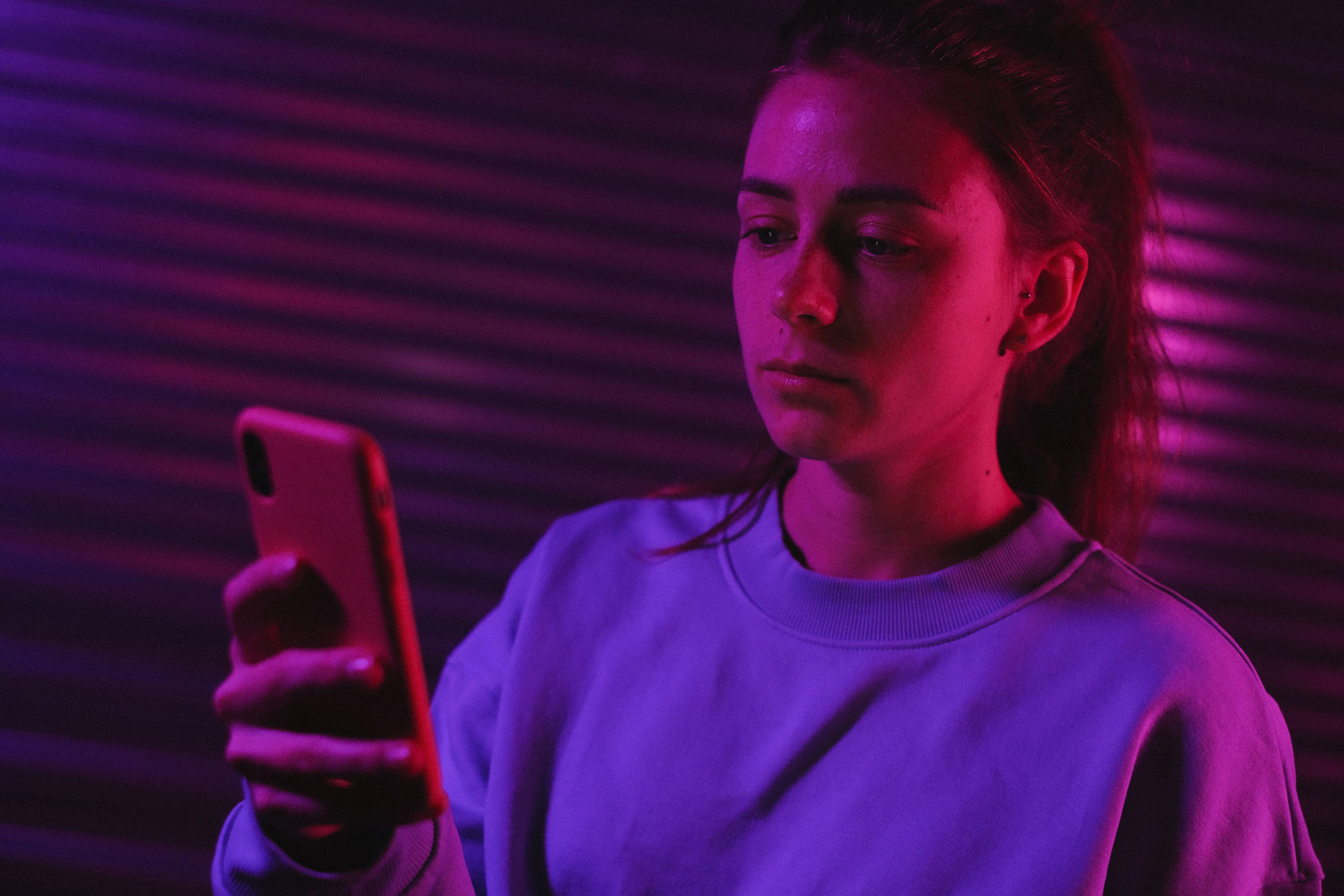 A young woman watching her phone in violet neon light